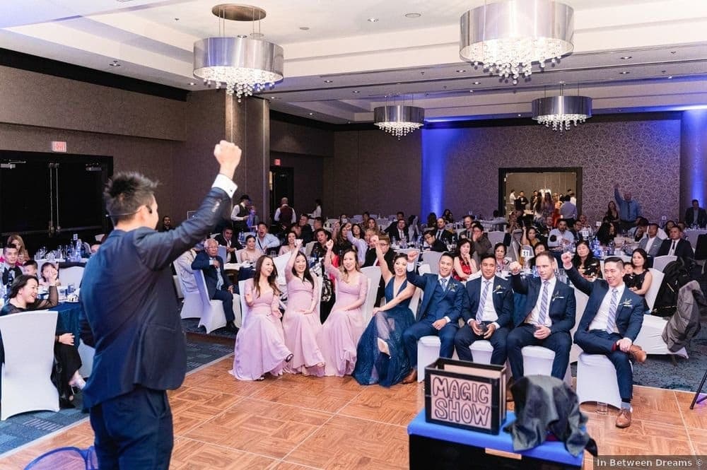 Kel with his arm raised on stage in front of a large seated wedding audience in Vancouver