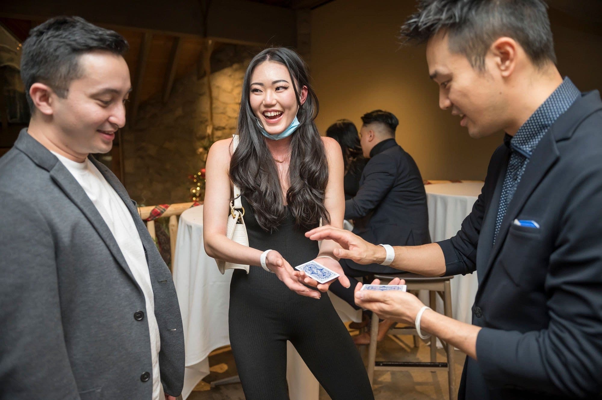 Kel performing close-up card magic for two laughing guests at a Vancouver holiday party
