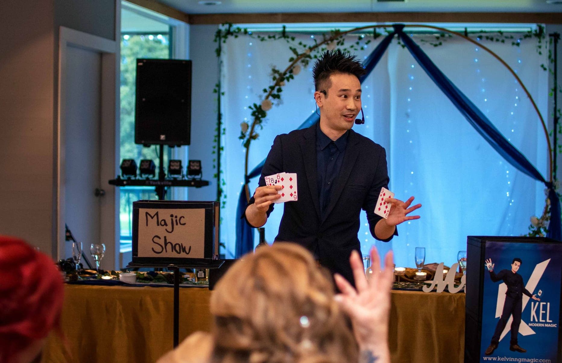 Kel holding a fan of cards beside a hand-lettered show sign at a country wedding in Hope, BC