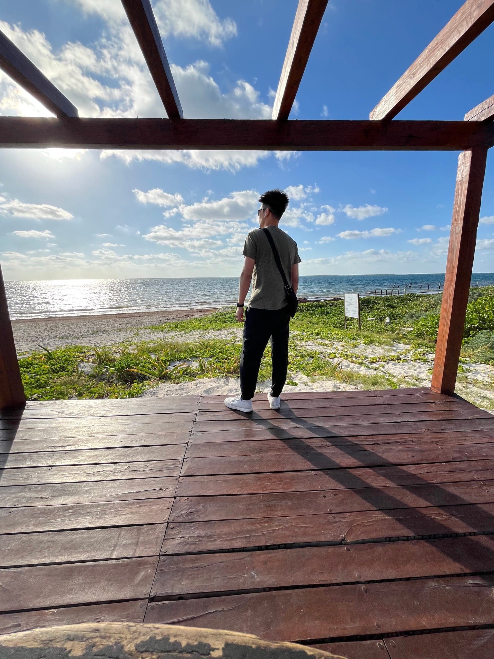 Kel standing at the end of a beach boardwalk looking out over the water