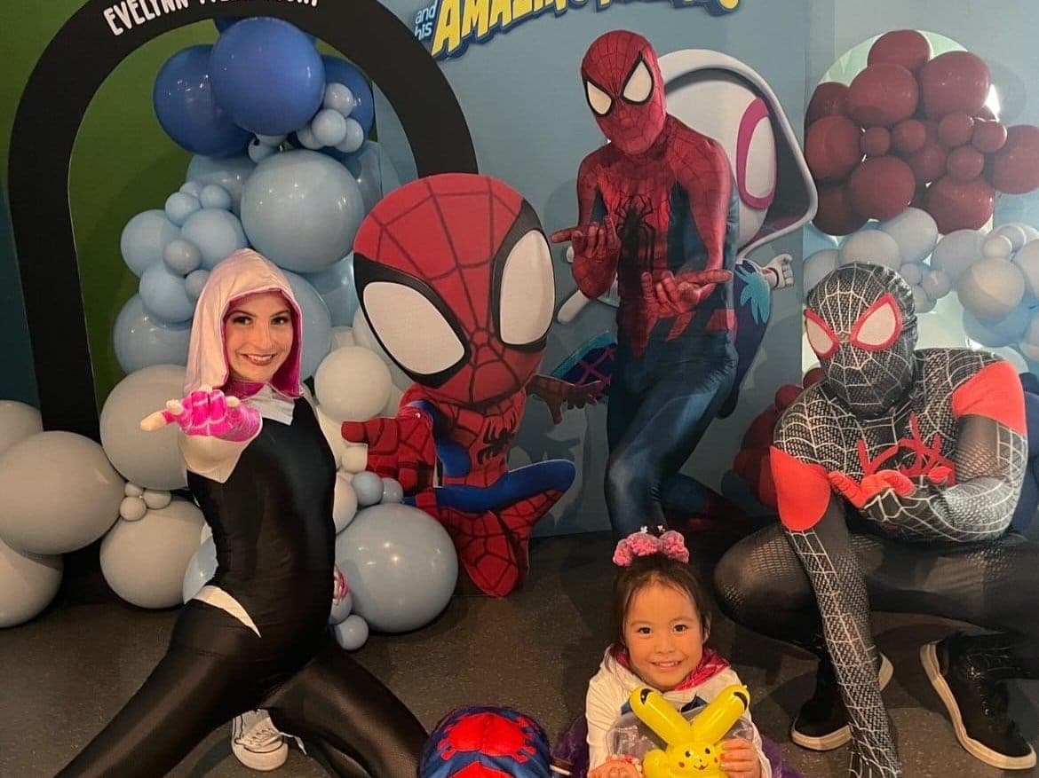 Costume characters from Dream Party Productions posing with a child at a themed balloon backdrop in Vancouver