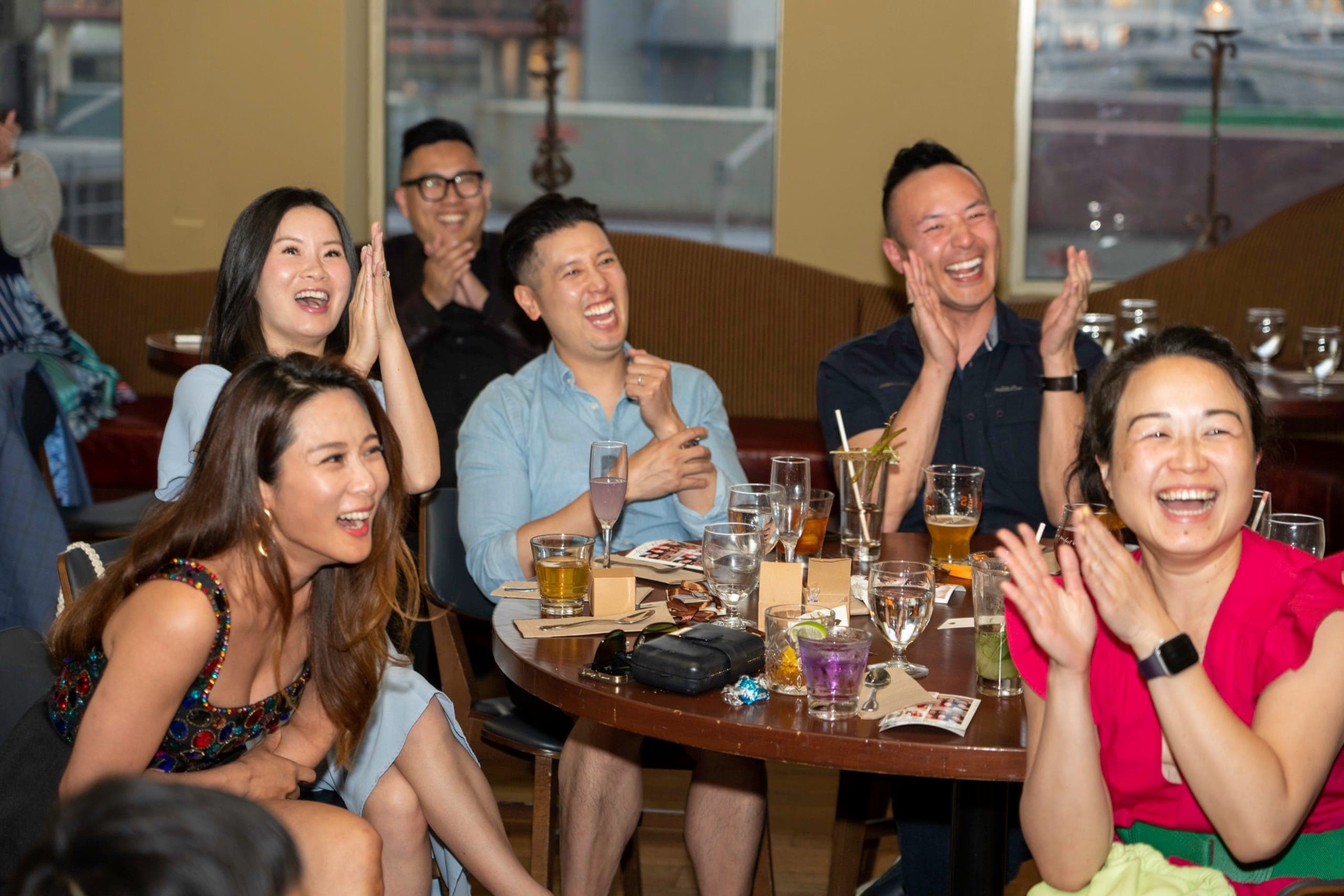 A table of guests laughing and applauding during close-up magic at a Vancouver restaurant
